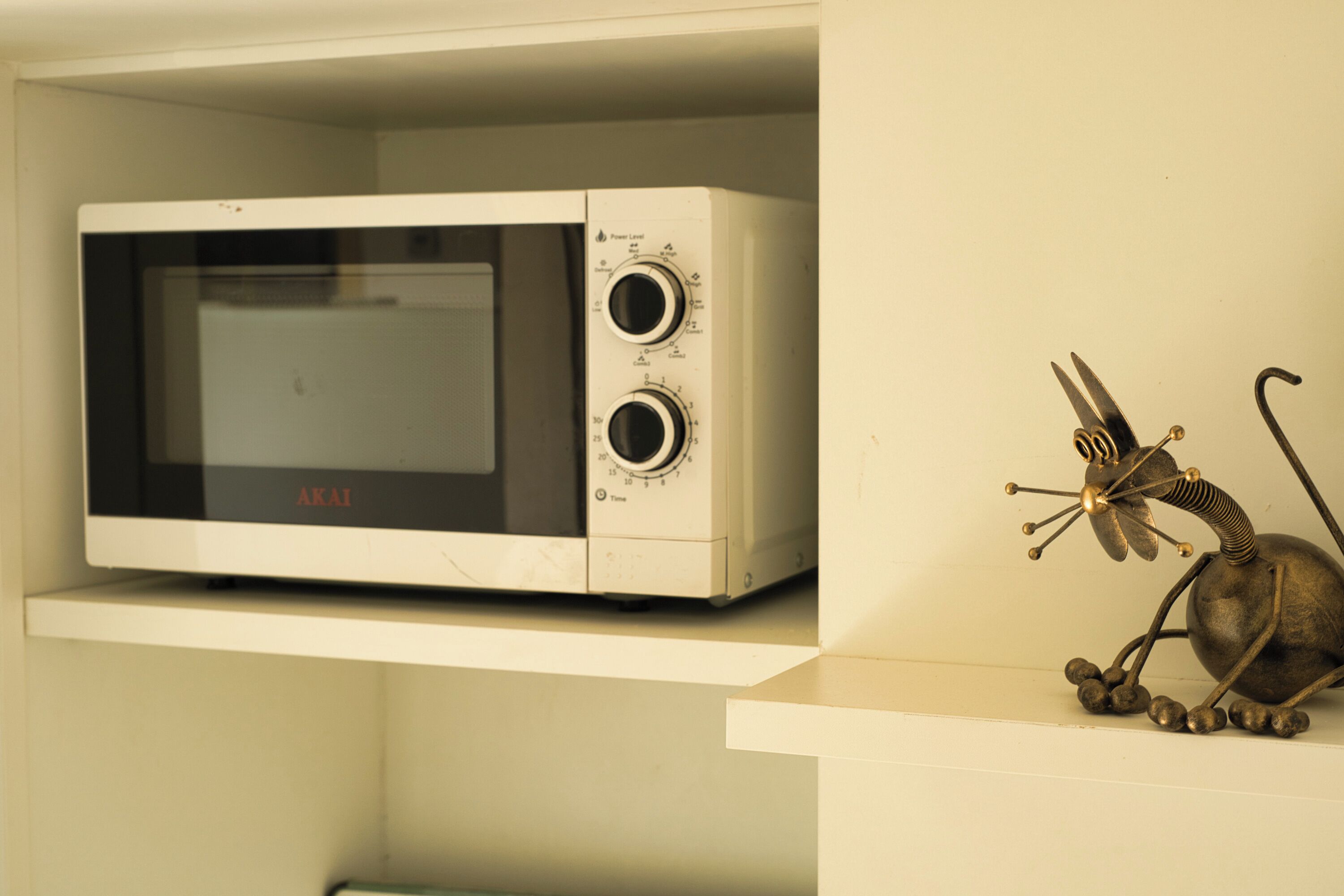 Un four à micro-ondes posé sur une  étagère, avec une sculpture métallique décorative à côté.