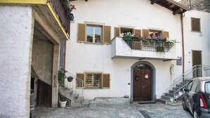 Un edificio con entrada empedrada en piedra, una puerta de madera y un balcón lleno de flores.
