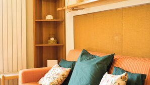 A cozy living room with a wooden bookshelf, a sofa with striped cushions, and a decorative shelf above the sofa. - Grigna Mountain View (Narro-indovero)