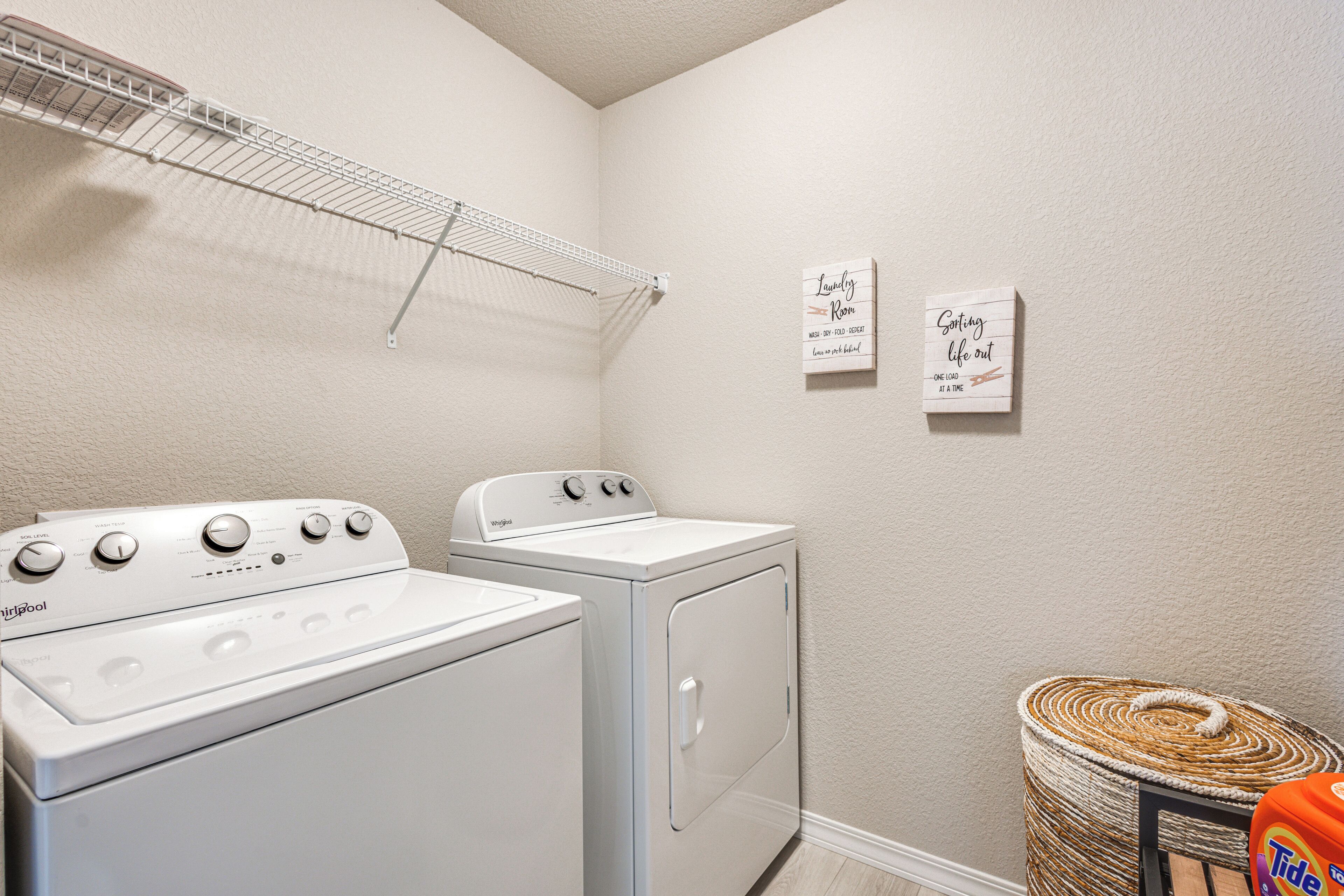 A laundry room with a Whirlpool washer and dryer, a drying rack, and two motivational signs on the wall.