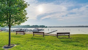Un espace vert avec des bancs et un arbre, d’où l’on a une vue sur une étendue d’eau calme, avec des bateaux amarrés au loin.