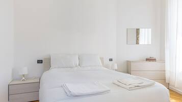 A neatly made bed with white linens, a bedside table with a lamp, and a nightstand with a lamp.