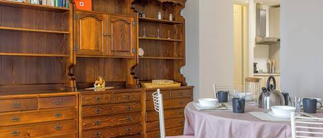 Un coin repas avec un buffet en bois, une table dressée pour deux personnes et une chaise.