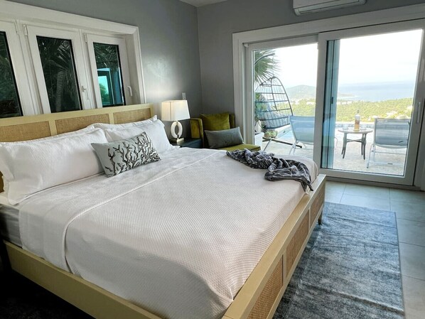 A bedroom with a large bed, a bedside table with a lamp, a chair, and a view of the outdoors.