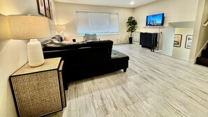 A modern living room with a black leather sofa, a standing lamp, a decorative vase, and a television on a stand.