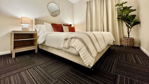 A neatly arranged bedroom with a bed, bedside table, lamp, and a potted plant.