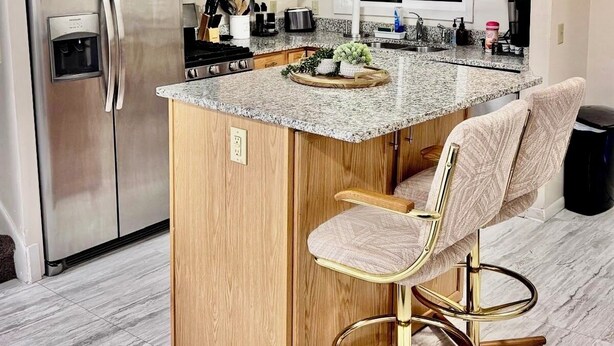 A modern kitchen with a central island, stainless steel appliances, wooden cabinets, and a bar stool.