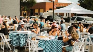 A crowded outdoor dining area with tables covered in checkered tablecloths and white chairs.