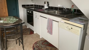 Cocina compacta con armarios blancos, encimera negra, lavavajillas Bosch y horno pequeño.