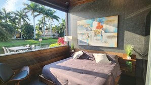A modern bedroom with a large bed, a dining area with a table and chairs, and a view of a garden with palm trees. - The duo of a prestigious holiday home and the comfort of a luxurious Motor Coach (Margate)