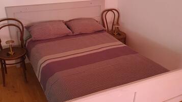 Una cama con colcha a rayas y almohadas, dos mesitas de noche con lámparas y un cabecero blanco.