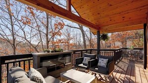 A covered outdoor deck with seating, a fire pit, and a view of trees.