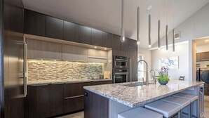 A modern kitchen with dark cabinetry, a granite countertop, and pendant lighting.