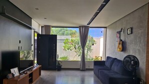 Un soggiorno moderno con una grande TV, un divano scuro e una ventola.