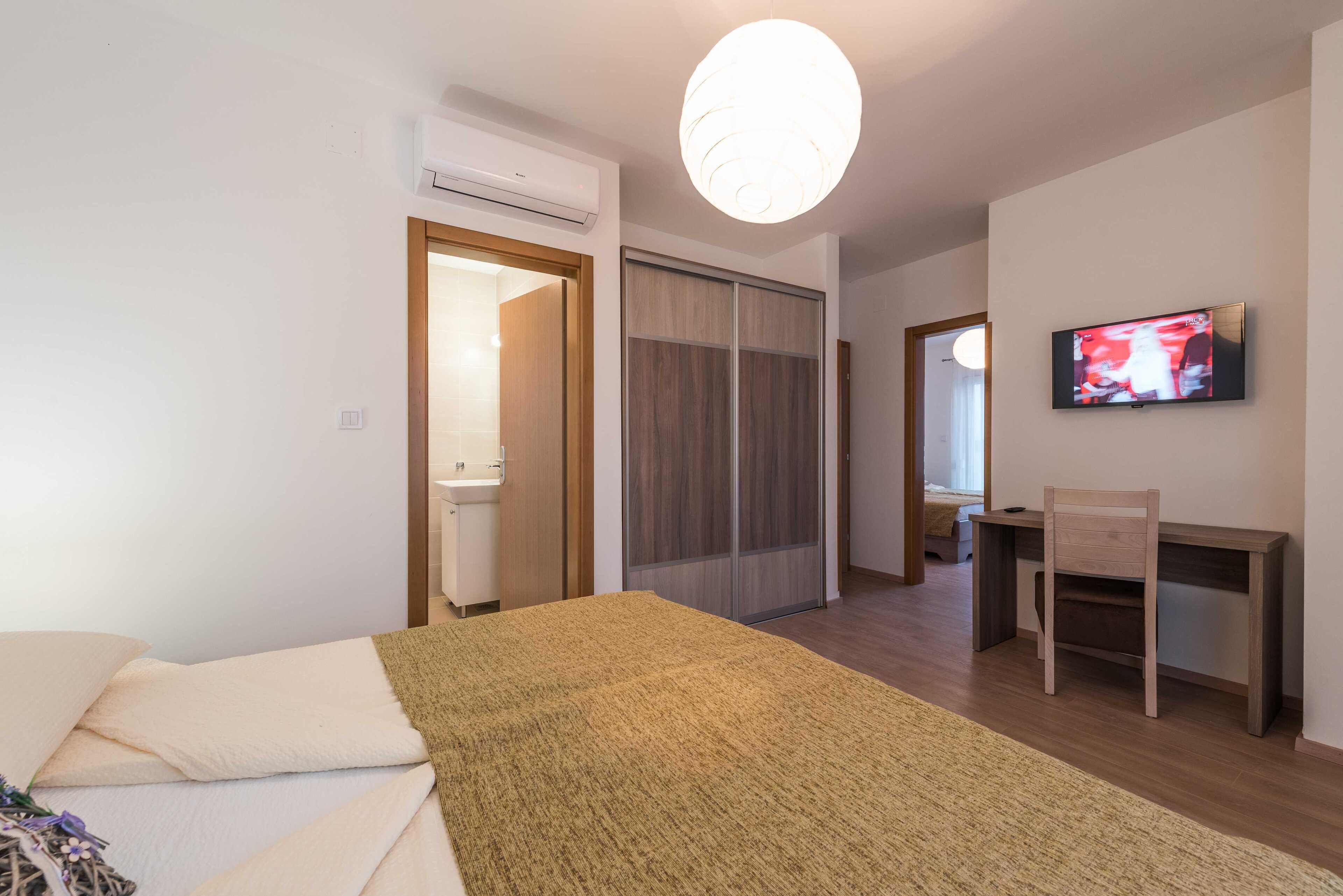 Ein Schlafzimmer mit einem Bett, einem Schreibtisch, einem Sessel, einem Fernseher und einem Kleiderschrank.