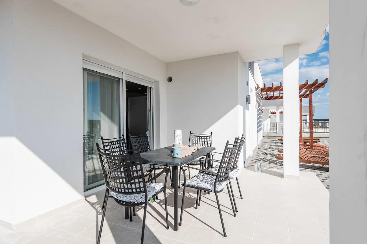 A patio with a table and chairs, a sliding glass door, and a view of the beach.