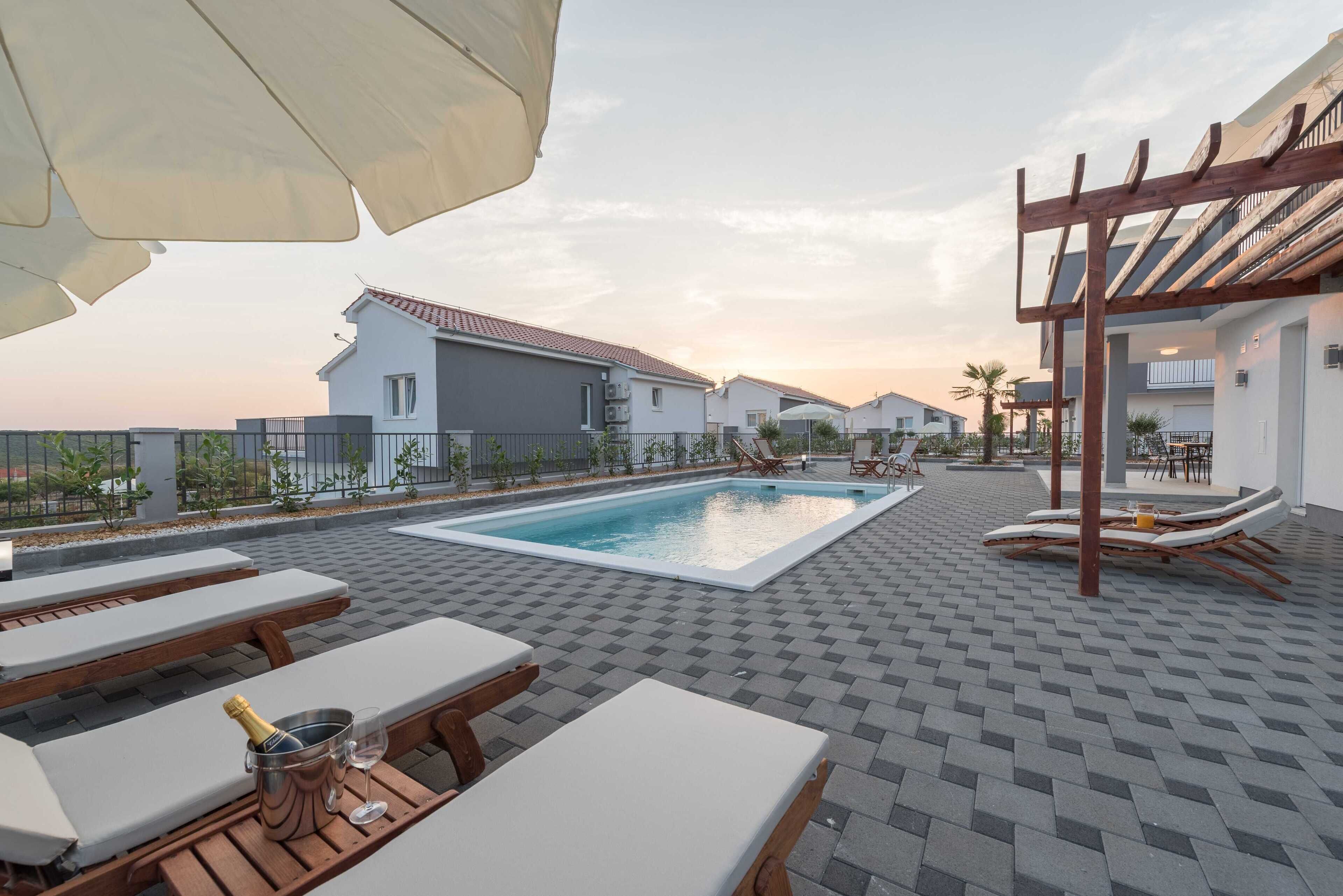 A rooftop pool area with lounge chairs, a pergola, and a view of residential buildings.