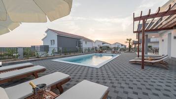 A rooftop pool area with lounge chairs, a pergola, and a view of residential buildings.