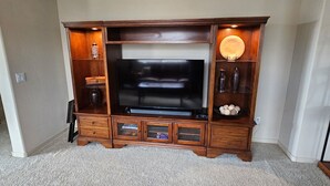 A living room with a large flat-screen TV, wooden entertainment center, and carpeted floor. - Charming 2-bedroom condo with WiFi, AC in lovely Fountain Hills (Fountain Hills)