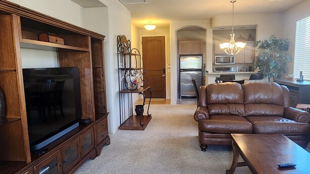 A spacious living room with a large flat-screen TV, leather sofa, wooden entertainment center, and a ceiling fan. - Charming 2-bedroom condo with WiFi, AC in lovely Fountain Hills (Fountain Hills)