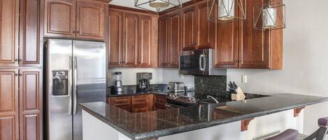 A kitchen with wooden cabinets, stainless steel appliances, granite countertops, and pendant lighting.