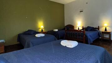 A hotel room with two beds, each with a blue bedspread and a white towel. There are two bedside tables with lamps.