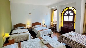 Een hotelkamer met vier bedden, houten hoofdeinden en een groot rondboogvenster met gordijnen.