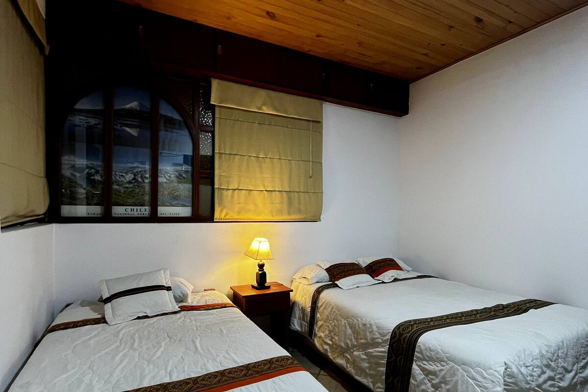 A room with two beds, a window with a view of mountains, and a wooden ceiling.