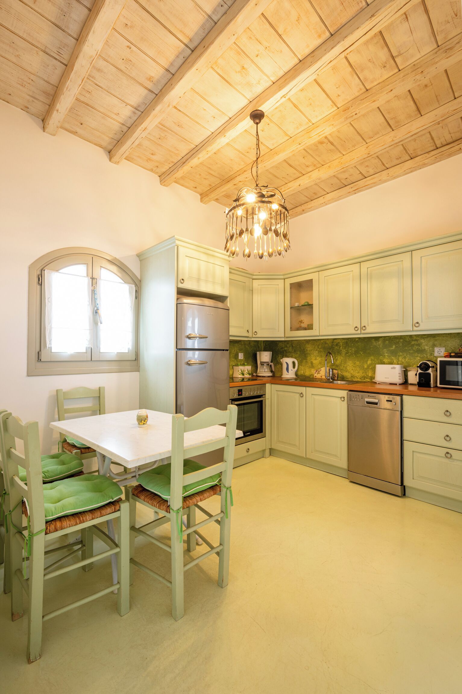 A kitchen with wooden ceiling beams, a dining table with chairs, and modern appliances including a refrigerator, oven, and dishwasher.