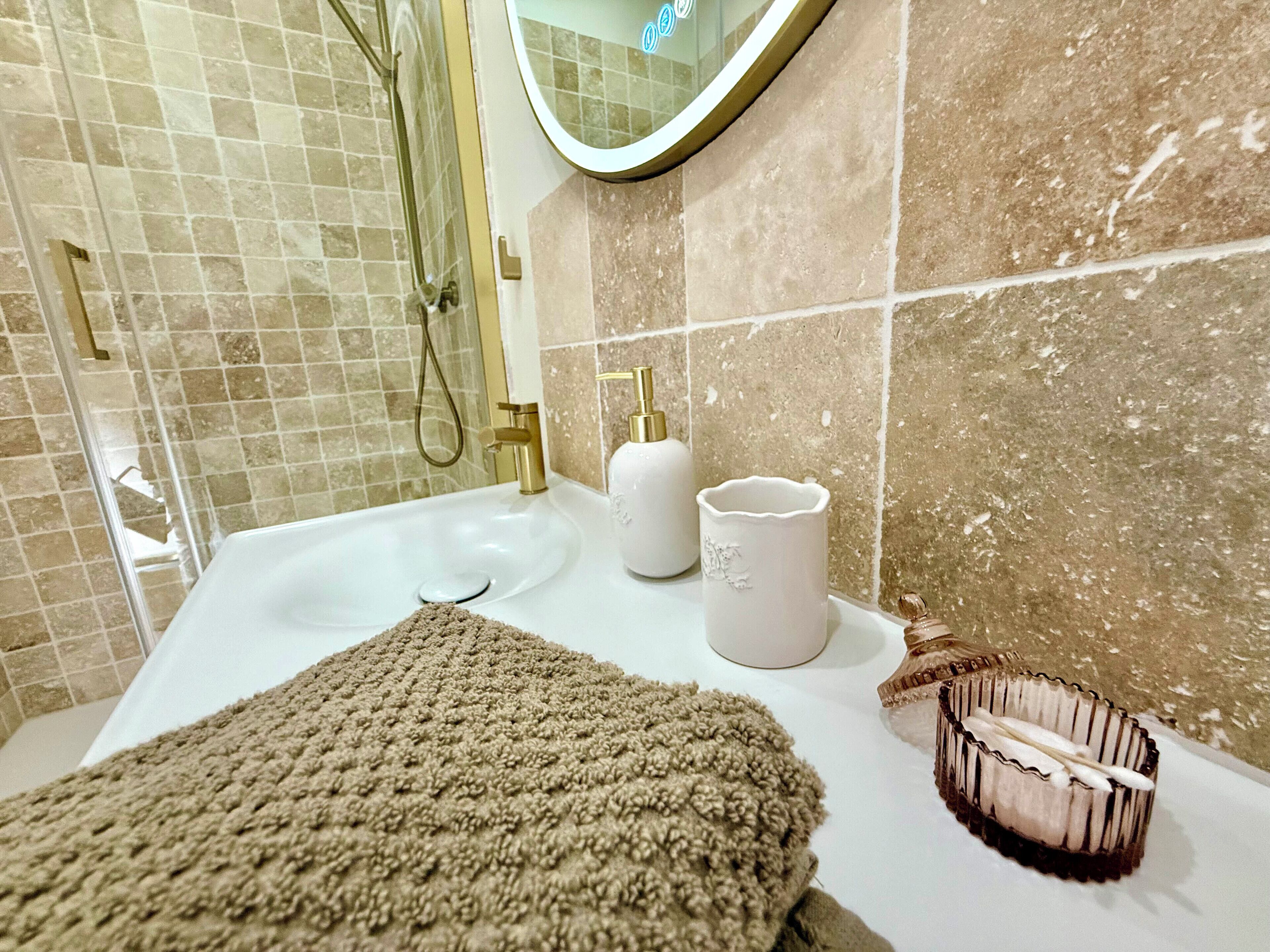 A bathroom with a white sink, gold fixtures, a beige towel, and a soap dispenser.