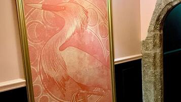A wall with a large, ornate painting of a bird, a stone archway, and a wall-mounted light fixture.