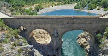 Un puente de piedra con tres arcos sobre un río, rodeado de vegetación y una pequeña zona de playa.