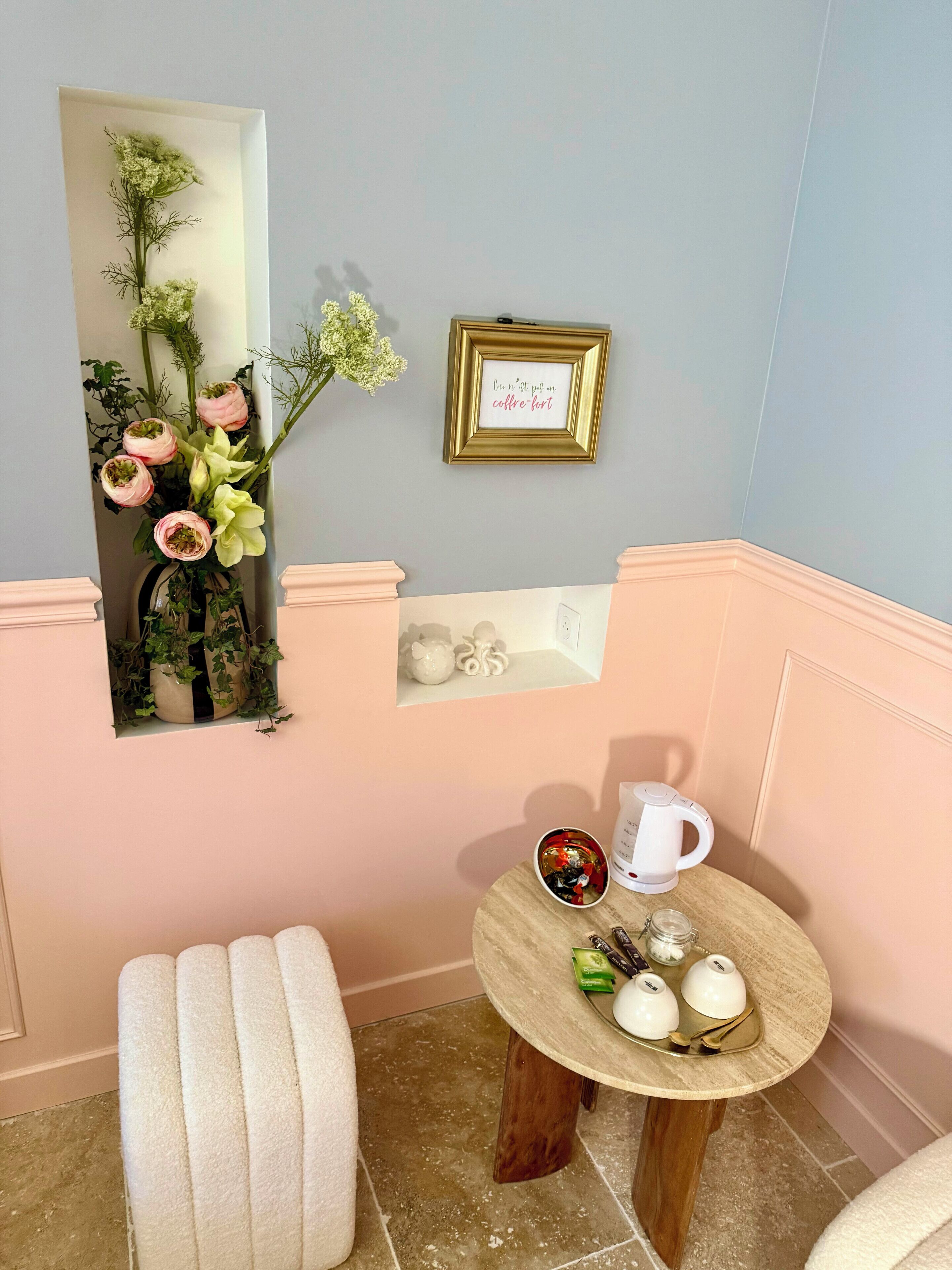 A room with a mirror, a small table with a coffee maker, and a cushioned bench.