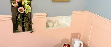 A room with a mirror, a small table with a coffee maker, and a cushioned bench.