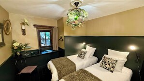 Hotelkamer met twee bedden, een kroonluchter, een raam met gordijnen en een kleine tafel met een plant.