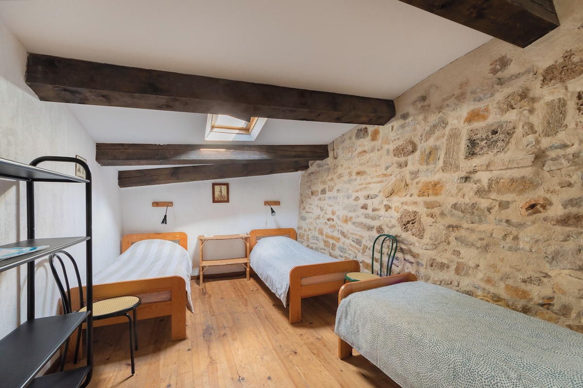 Een kamer met twee houten bedden, een bureau en een stoel. Boven de bedden bevindt zich een dakraam en aan de zijkant een stenen muur.