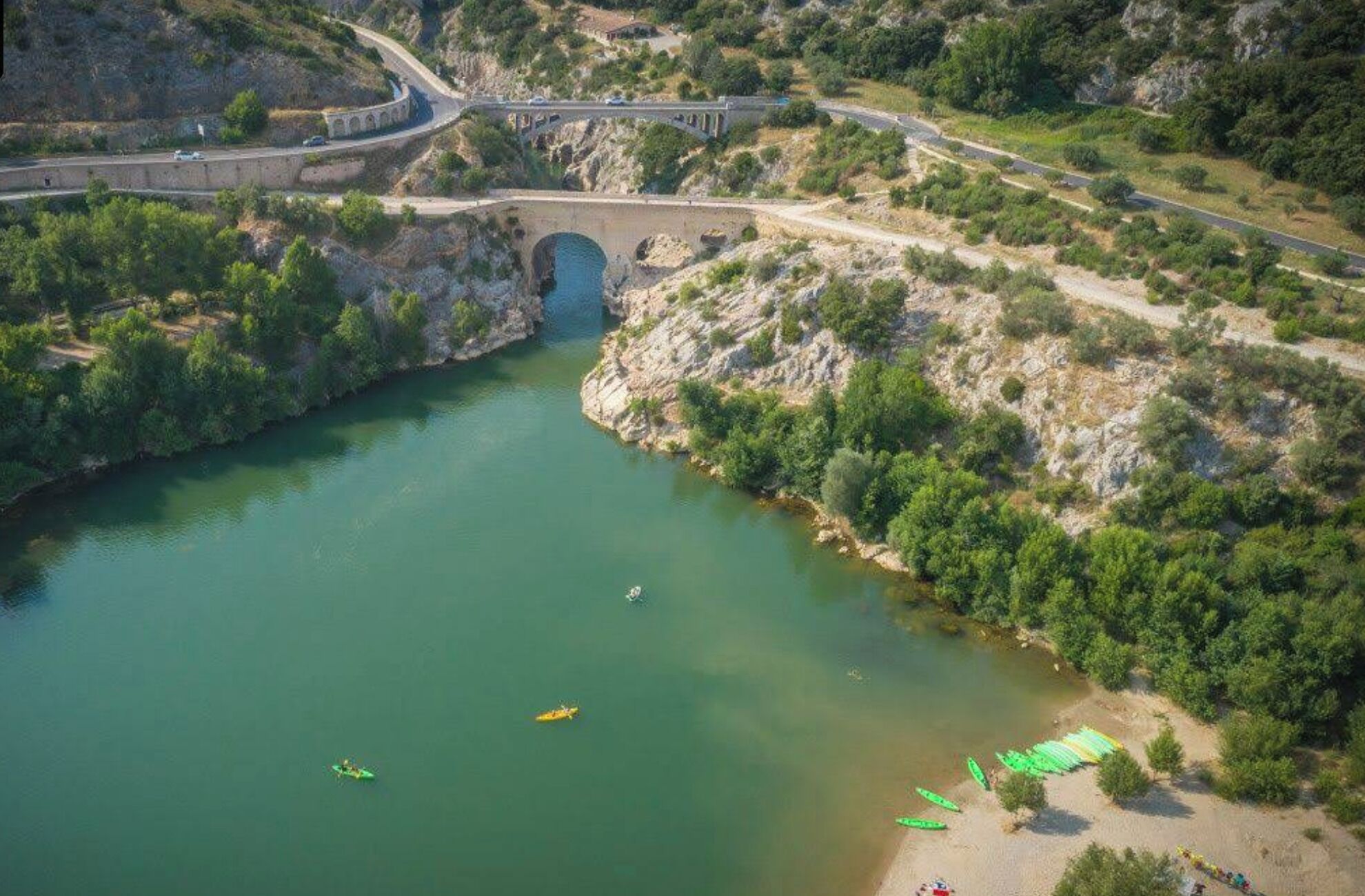 Eine Luftaufnahme eines Flusses mit einer Brücke, Booten und einem Strand mit Kanus.
