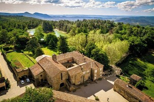 Edificio histórico de piedra con un patio, rodeado de abundante vegetación y un río.