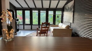 A modern living room with a wooden dining table, a sofa, and a chair. Large windows provide a view of greenery outside. - Vacation home with beautiful garden near Loreley and Middle Rhine Valley (Bogel)