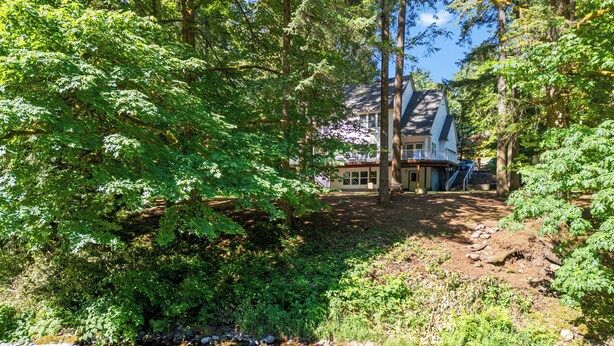 A house surrounded by dense forest with a clear stream in the foreground. - Peaceful Forest Riverfront Escape near PDX w/ Hot Tub, Kayaks, & River Access (Washougal)