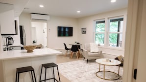 A modern kitchen with a central island, bar stools, a dining area with a round table and chairs, and a large window with a view of greenery. - Peaceful Forest Riverfront Escape near PDX w/ Hot Tub, Kayaks, & River Access (Washougal)