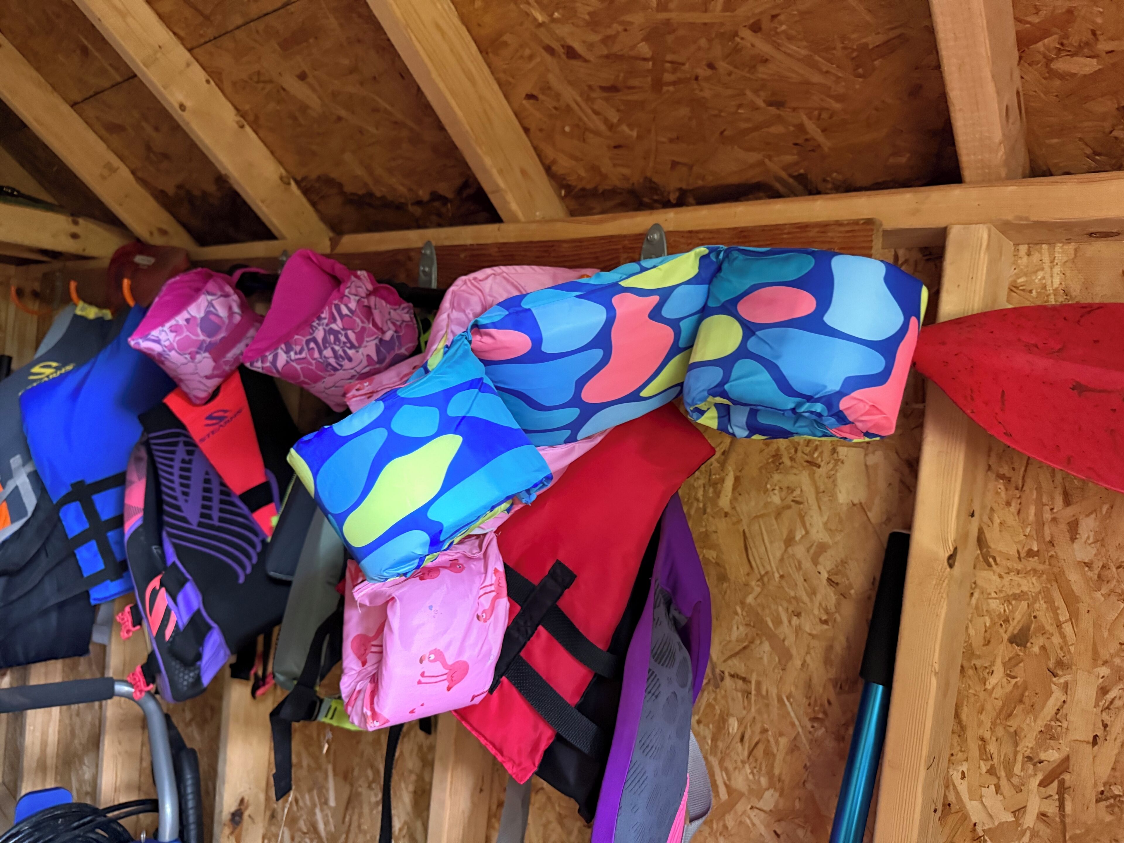 Une rangée de gilets de sauvetage colorés est accrochée à un mur en bois.