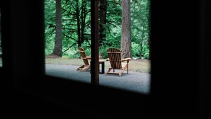 A view from inside a cabin looking out to a forest with two Adirondack chairs and a table. - Peaceful Forest Riverfront Escape near PDX w/ Hot Tub, Kayaks, & River Access (Washougal)