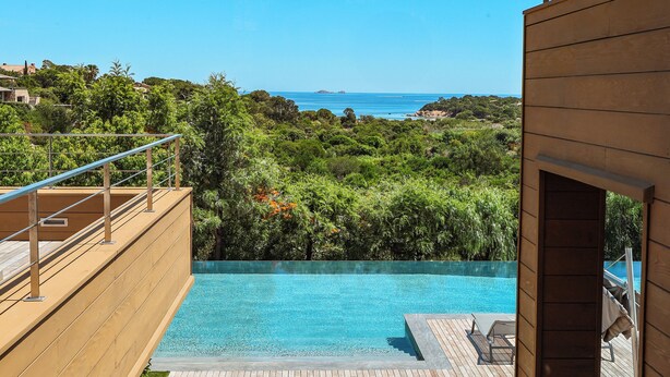 A modern pool area with a view of the sea and surrounding greenery.