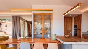 A modern kitchen with a central island, bar stools, and a wooden cabinet with glass doors.