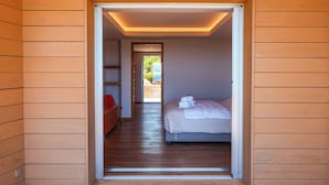 A modern hotel room with a wooden floor, a bed with white linens, and a red chair.