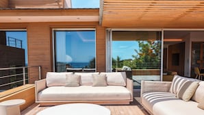 A modern outdoor living area with a wooden deck, a white sofa set, and a round table.