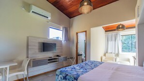 A bedroom with a bed, a desk, a chair, a TV, and a window.
