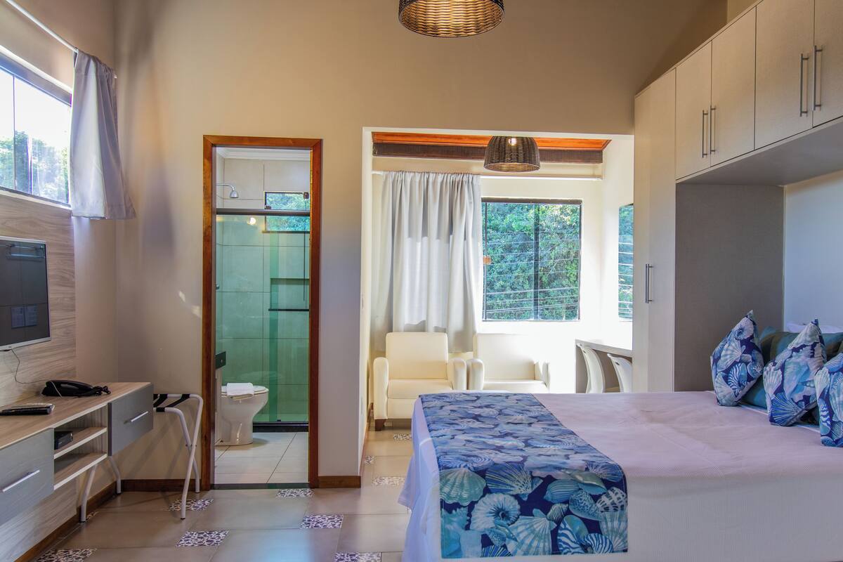 A bedroom with a bed, a desk, a chair, a wardrobe, and a bathroom with a toilet and shower.
