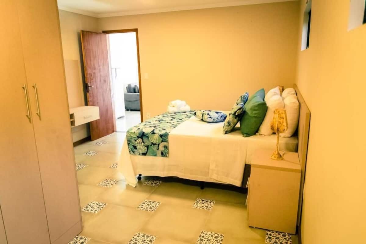 A bedroom with a bed, a nightstand, a wardrobe, and a door leading to another room.